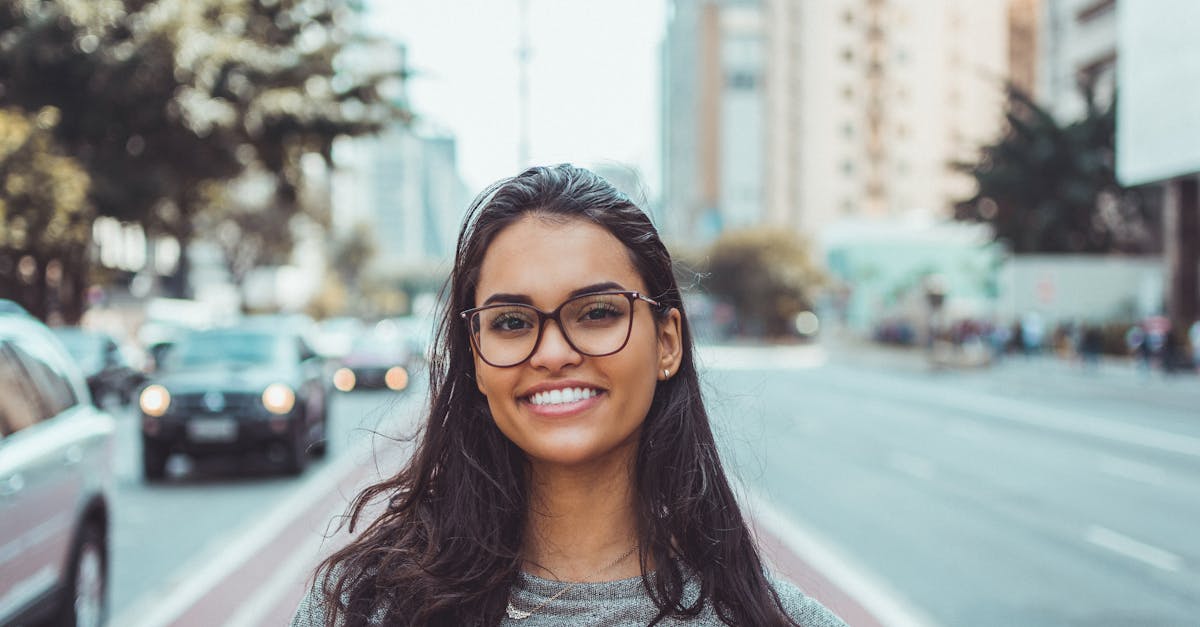 A young woman with glasses smiling on a city street, embracing urban lifestyle.