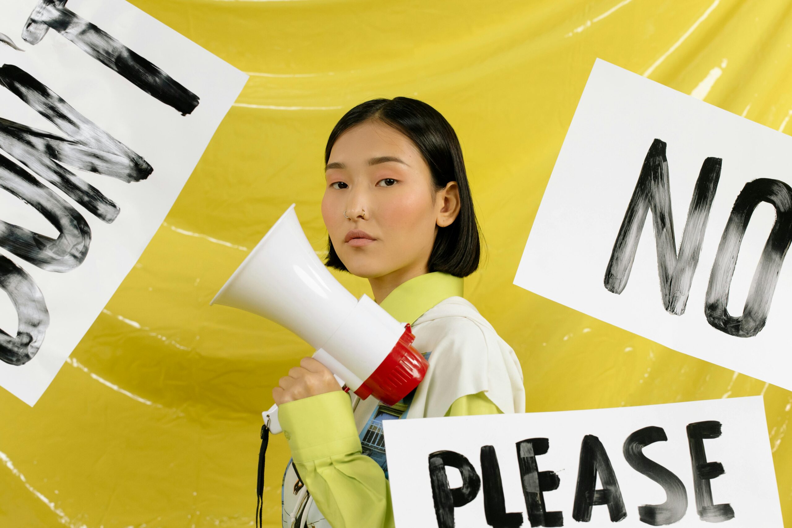 Portrait of a young activist holding a megaphone against a yellow background surrounded by protest signs.