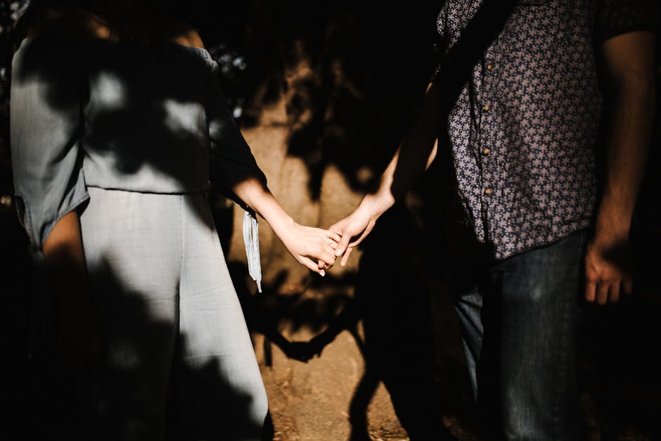 Romantic couple holding hands, capturing intimate shadows and sunlight outdoors.