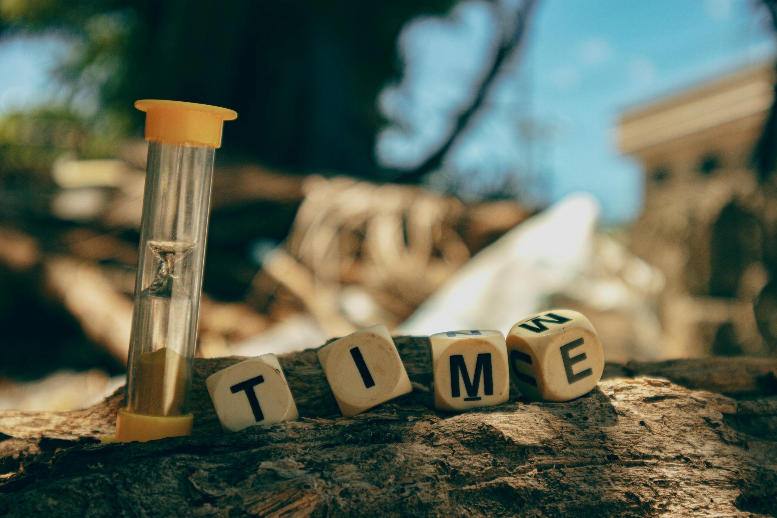 Hourglass and wooden blocks with letters spelling 'TIME' on a sunny day outdoors.