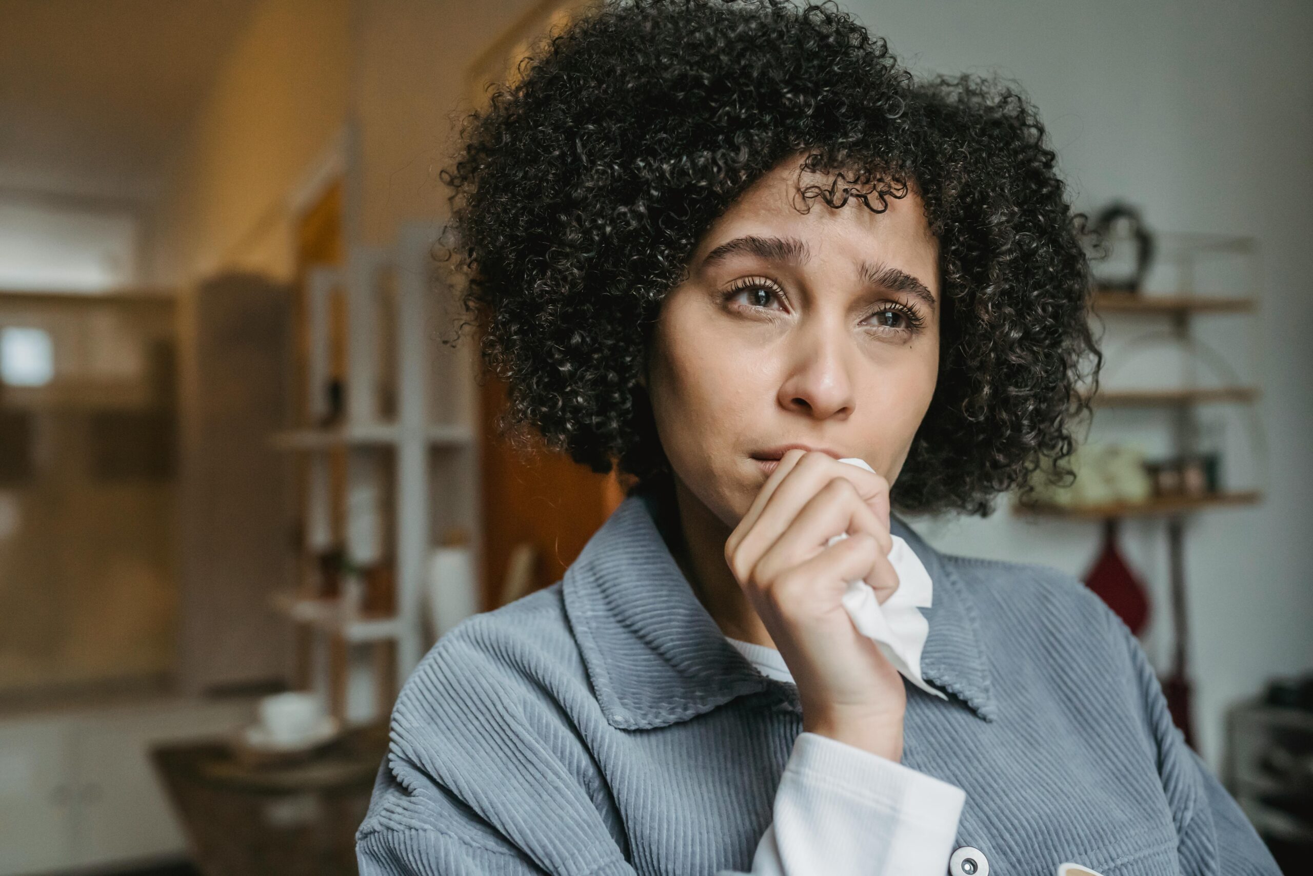 Unhappy African American woman with Afro hairstyle touching chin with tissue while looking away with sorrow