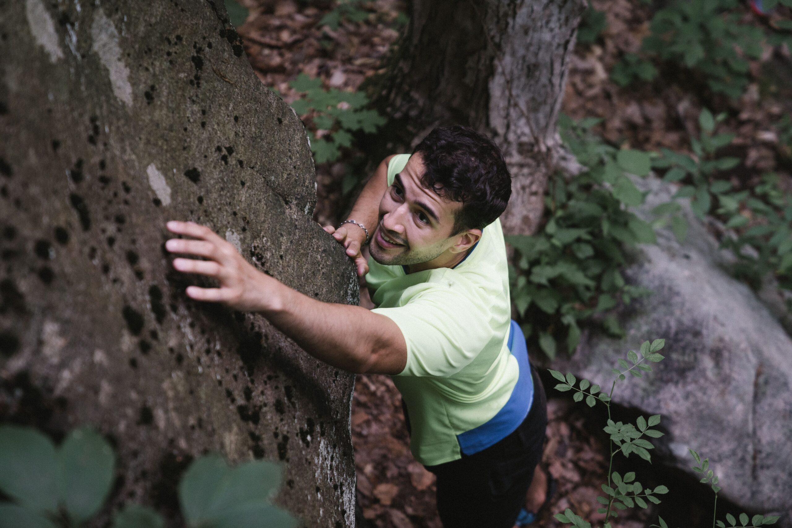 A man climbs a rock in a vibrant forest setting, showcasing adventure and nature.
